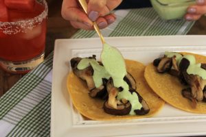 Hand drizzling sauce on mushroom vegetarian tacos.
