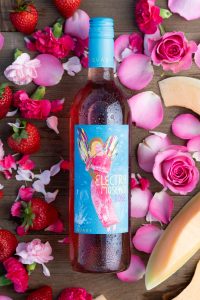 Bottle shot of the new Electra Moscato Rosé surrounded by flowers, roses fresh strawberries and melon.
