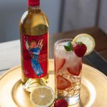 A bottle of Quady Electra Moscato next to a strawberry lemonade moscato cocktail on ice.