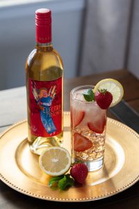 A bottle of Quady Electra Moscato next to a strawberry lemonade moscato cocktail on ice.