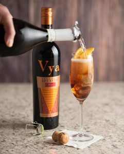 A champagne flute with vya sweet vermouth inside and a bottle of prosecco being poured into it to make the sparkling vya cocktail.