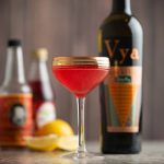 Scofflaw cocktail in a gold rimmed coupe glass with bottles of vya extra dry vermouth, grenadine syrup, regans orange bitters and a lemon behind it.