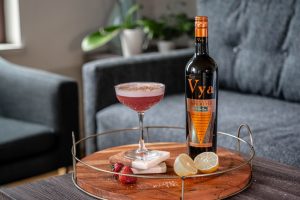 Berry sour cocktail created by Beautiful Booze sitting on a coffee table next to a bottle of Vya Extra Dry Vermouth.