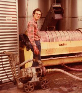 Vintage photo of Andrew Quady making wine and standing next to a wine pump and press.