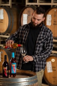 Evan Collins, Laboratory Tech. at Quady Winery, pouring Electra Moscato wine into a wine glass.