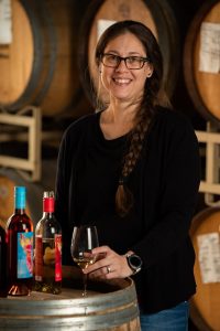 Andrea Milliorn, Senior Accountant at Quady Winery, holding a glass of Electra Moscato while resting on a wine barrel.