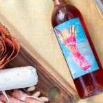 Bottle of Electra Moscato Rosé on a picnic blanket next to a charcuterie board.