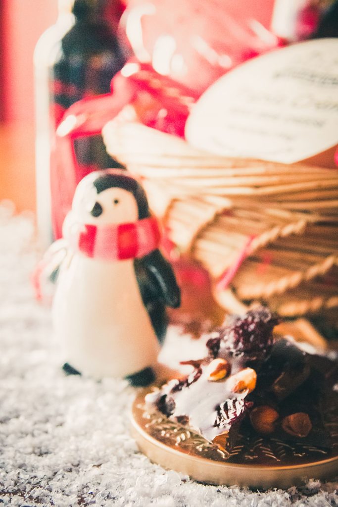 Chocolate pieces with raisins and nuts next to a penguin figurine and a sweet wine gift basket