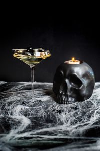 El Esqueleto Mezcal Halloween cocktail with black skull, a candle and spiderwebs