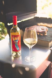 Electra Moscato in a glass and in a bottle, next to a barbecue with ribs on the grill