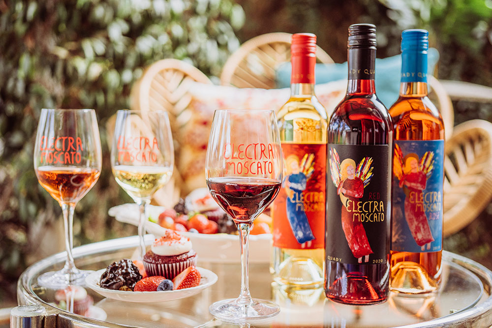 Quady Electra Moscatos with glasses of each wine and a plate with a cupcake and fruit