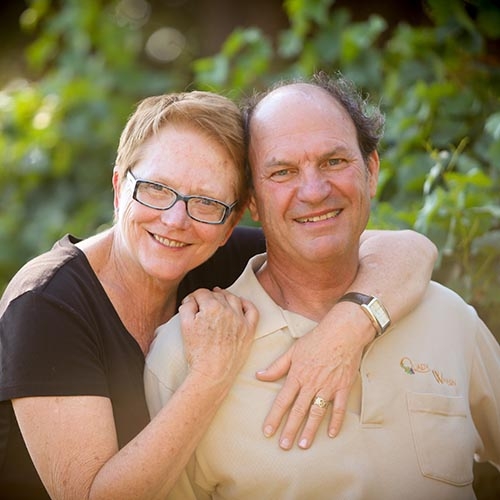 Andrew and Laurel Quady holding each other in front of a vineyard at Quady Winery in Madera, California.